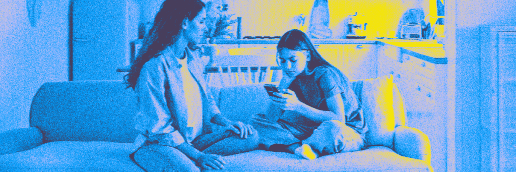 checked out teen girl looking at her cell phone with her mom sitting with her on a couch